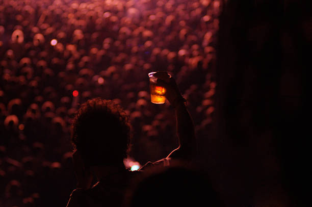 En la imagen se puede ver como poco definido unos fuegos artificiales típicos de conciertos y una persona que solo llega a verse su silueta con una cerveza en la mano, se puede ver que es mjuy de noche por lo oscuro que está el cielo.