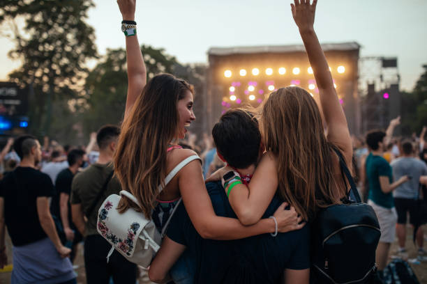 En la imagen se observa unos amigos o personas en un festival que están juntos abrazándose y disfrutando del festival de música en el que están, es mediodía anocheciendo.