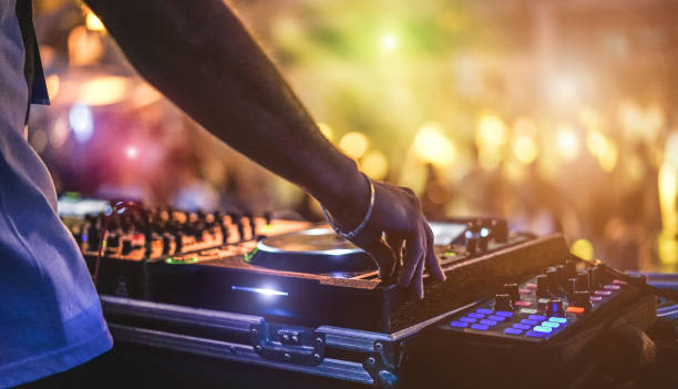 En la imagen se puede observar un dj con su equipo tocando algo de música a una audiencia que aparece en la imagen desenfocada.