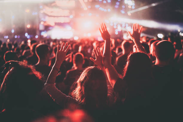 La imagen muestra una multitud en un festival aparentemente de noche, están enfrente de un escenario el.