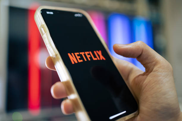 En la imagen es visible un teléfono sujetado por una mano, la persona que tiene el teléfono está entrando a la aplicación de streaming Netflix en el móvil.