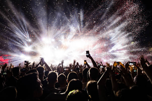 En la imagen se ve una multitud de gente en un festival enfrente de un escenario, se ve que hay muchas luces y confeti