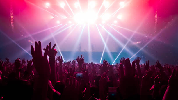 En la imagen se puede ver una multitud  de gente frente a un escenario, están ambientados con luces de colores neón.