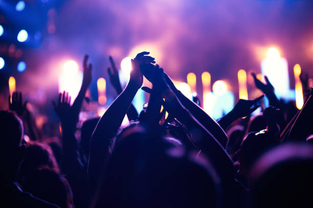 En la imagen se observa una multitud alzando las manos en un festival, están rodeados de luces color neón.
