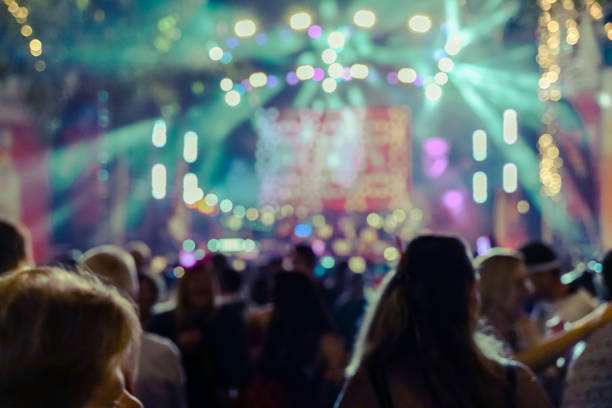 En la fotografía se ve una multitud en frente de un escenario, se puede ver que es de noche y están ambientados con unas luces de muchos colores