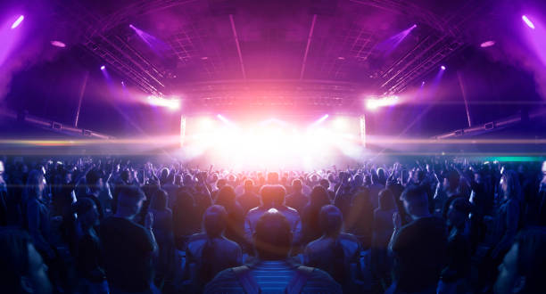 En la imagen se ve una multitud enfrente un escenario rodeados de luces neón