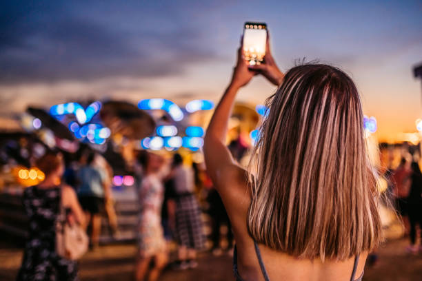 En la imagen aparece una chica sacando una fotografía de donde está con su móvil, ella está en lo que parece un festival 