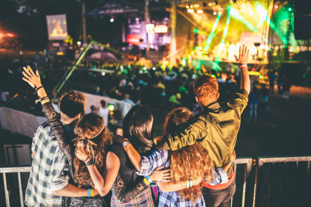 En la imagen se puede ver una multitud enfrente de un escenario poco visible, debido a que se difumina en la imagen ya que se enfoca en un grupo de amigos que también están disfrutando del festival. 