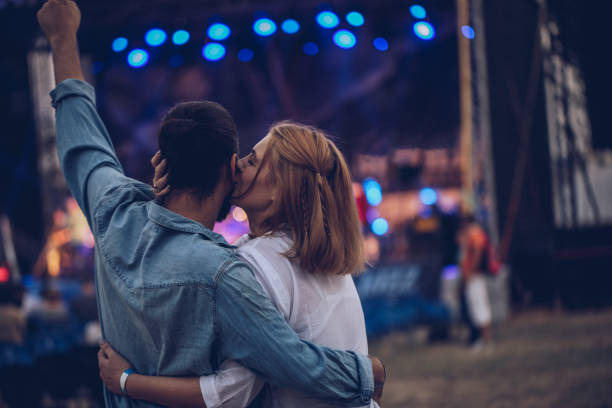En la imagen puede verse una pareja en un festival abrazándose y en el fondo logra verse un escenario.
