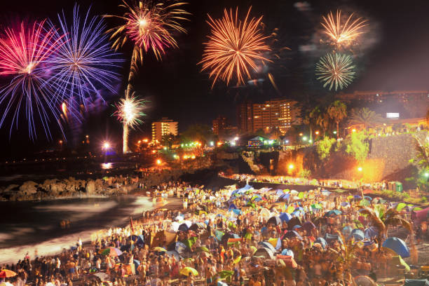 En la imagen se puede ver en una playa de España un festival, hay una multitud de gente a la orilla del mar pasándolo bien y viendo los fuegos artificiales en la noche